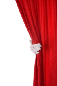 Red curtain being held open by a hand with a white glove on it